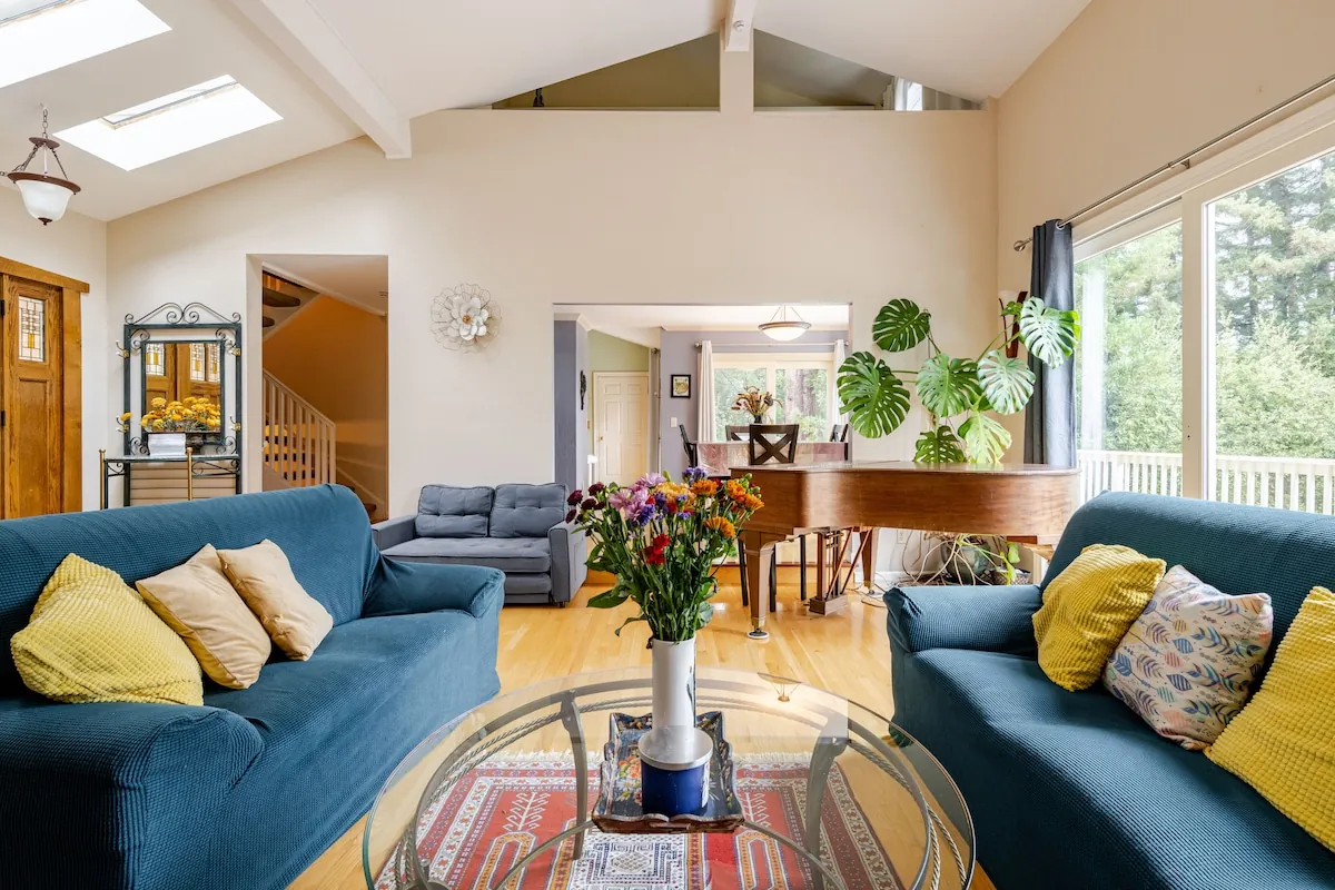 Living room with grand piano, vaulted ceilings, and skylights